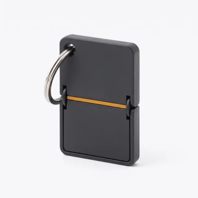 A charcoal split-flap tile keychain charm with an amber line